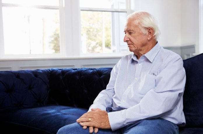 Depressed Senior Man Sitting On Sofa At Home