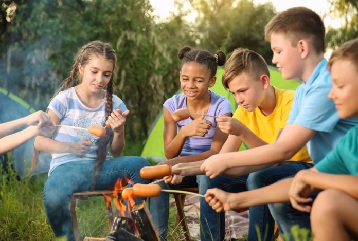 Group of children cooking sausages on campfire